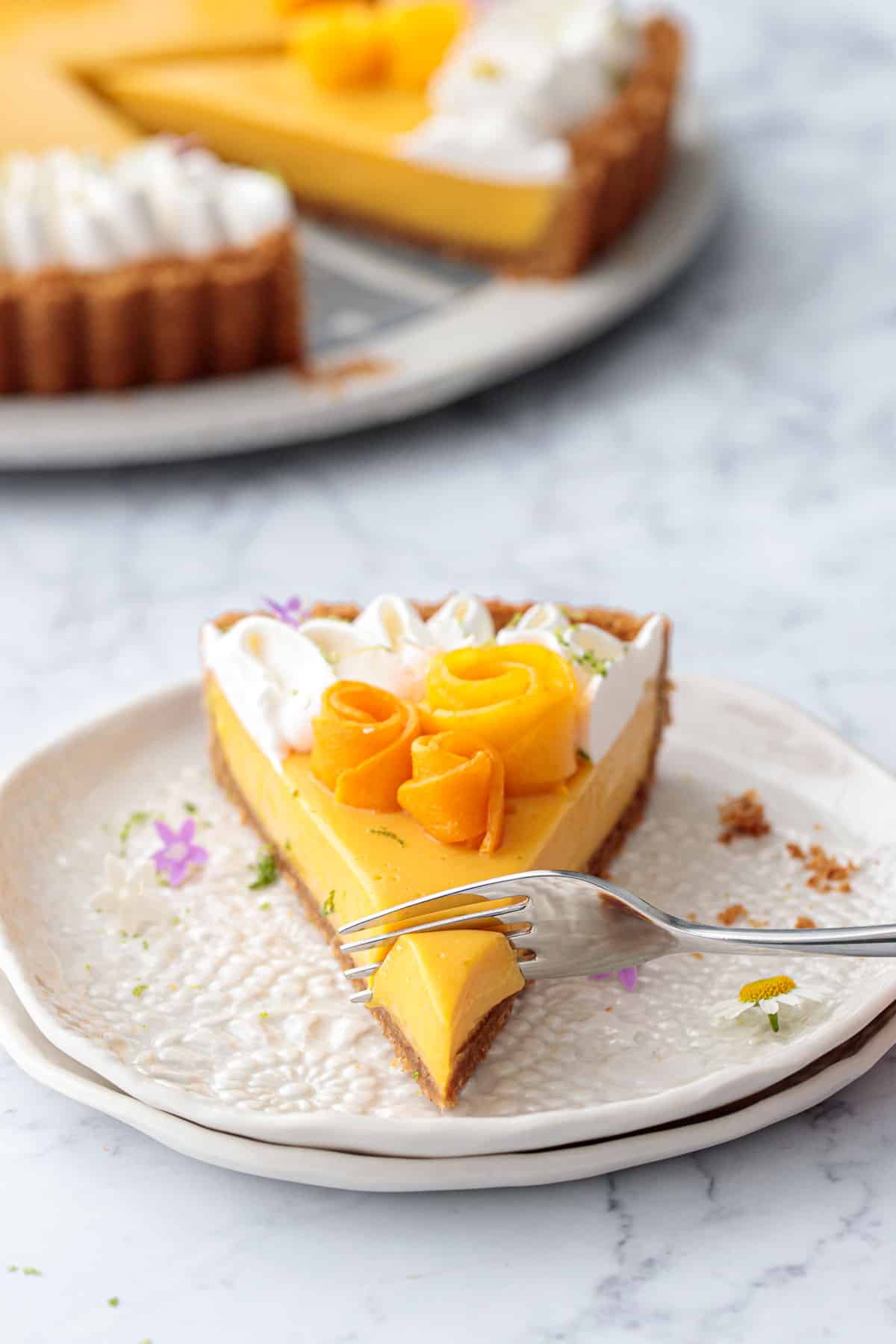 Fork cutting into a slice of Mango Lime Tart on a white lace plate.