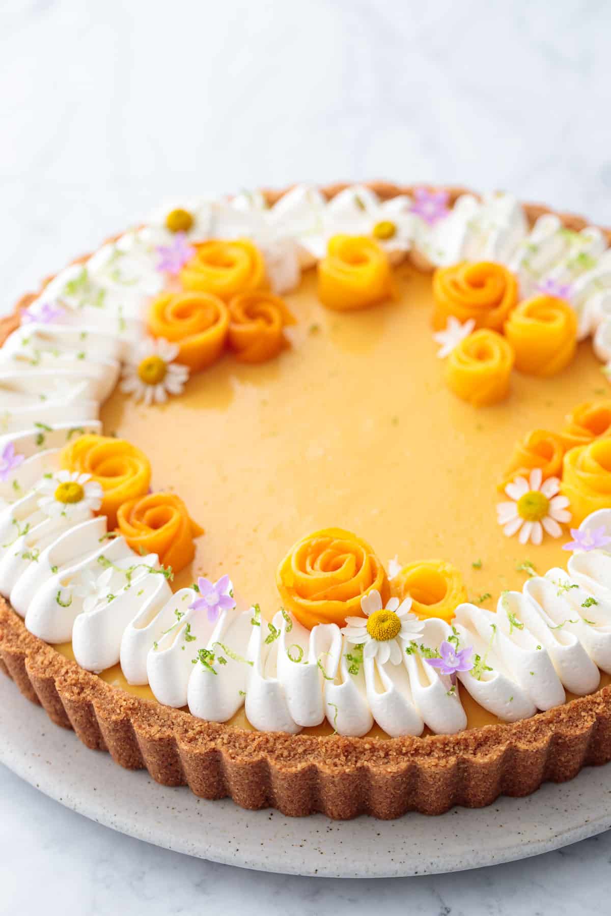 Closeup of a Mango Lime Tart with edible flowers and mango flowers for decoration.