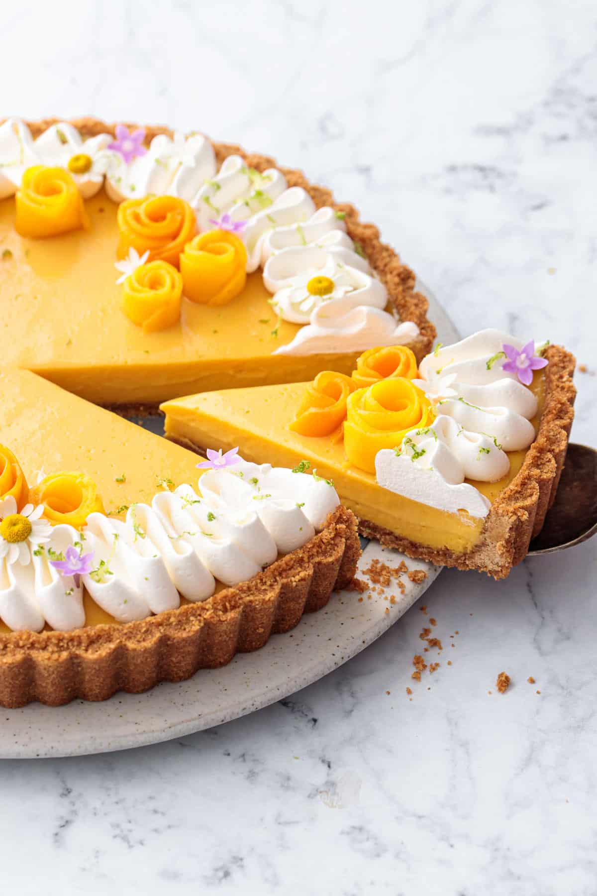 Slice of Mango Lime Tart showing the creamy texture and bright yellow color of the filling, decorated with whipped cream and edible flowers.
