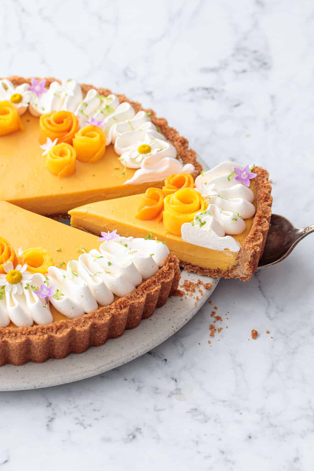 Cut slice of a Mango Lime Tart on a plate, decorated with a squiggle of whipped cream and edible flowers.