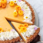 Mango Lime Tart with a slice cut out of it to show the creamy texture inside, decorated with whipped cream and edible flowers.