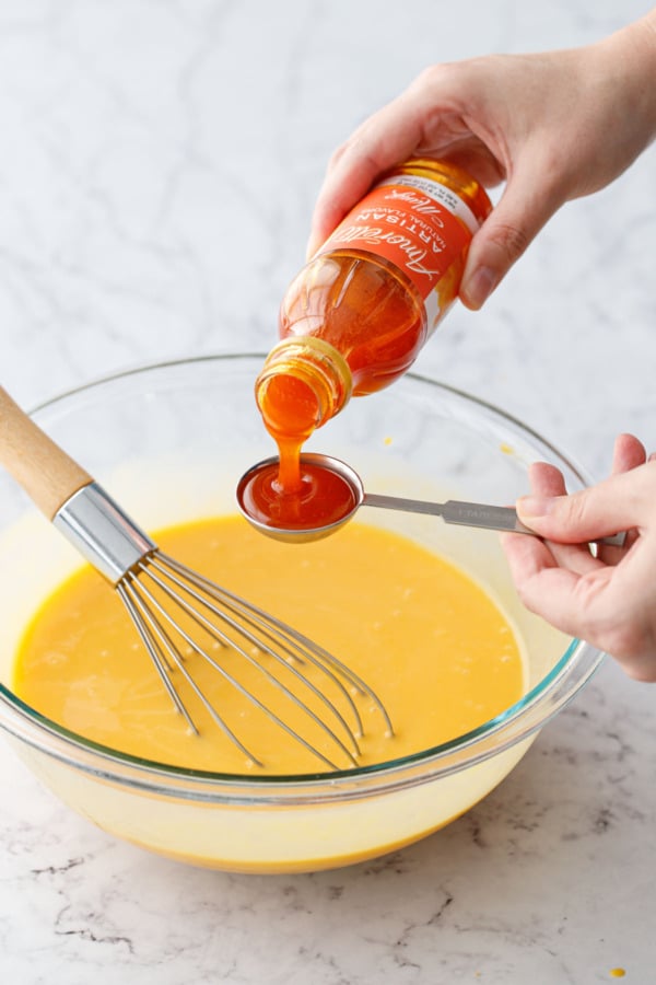 Pouring Amoretti Natural Artisan Mango flavoring into a tablespoon measuring spoon.