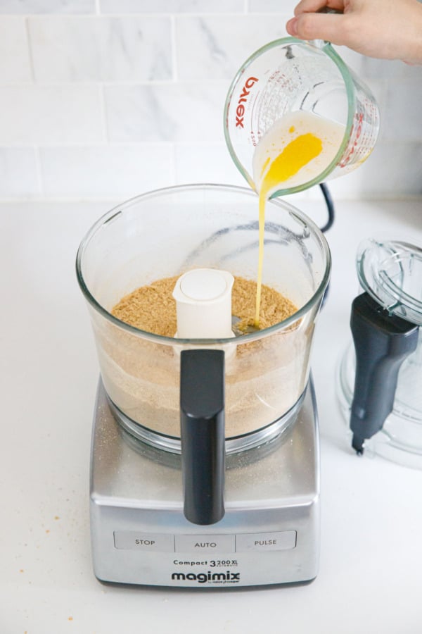 Drizzling melted butter into food processor with graham cracker crumbs.