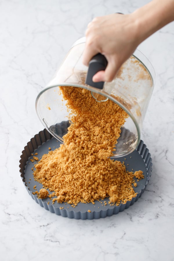 Pouring graham cracker crumbs from the food processor into the tart pan.