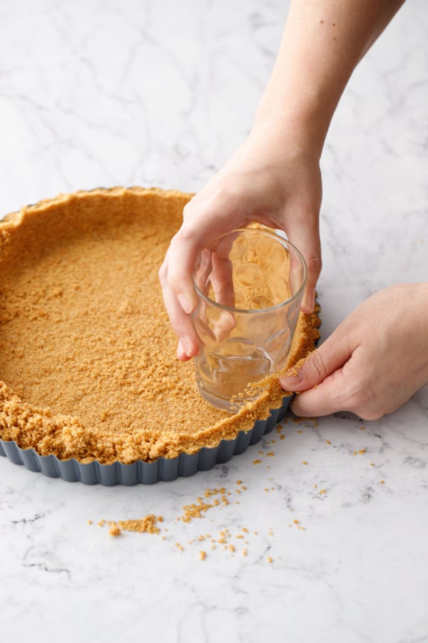 Using a juice glass to shape the graham cracker crust in the tart pan.