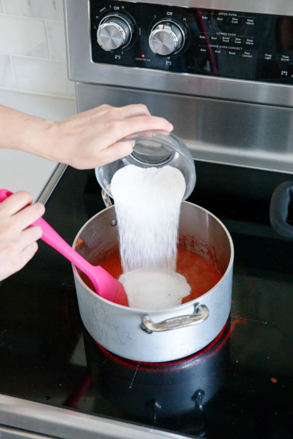 Adding sugar and pectin mixture to saucepan with boiling fruit.