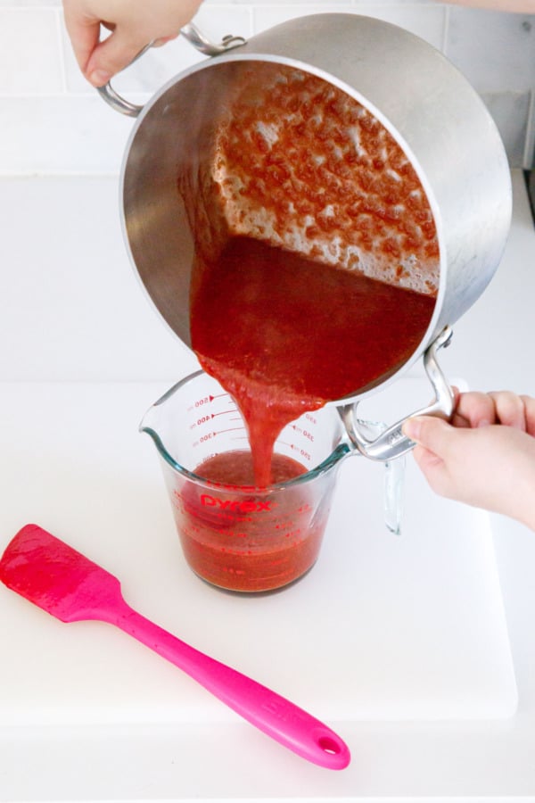 Pouring finished cooked jam from saucepan into a glass measuring cup.
