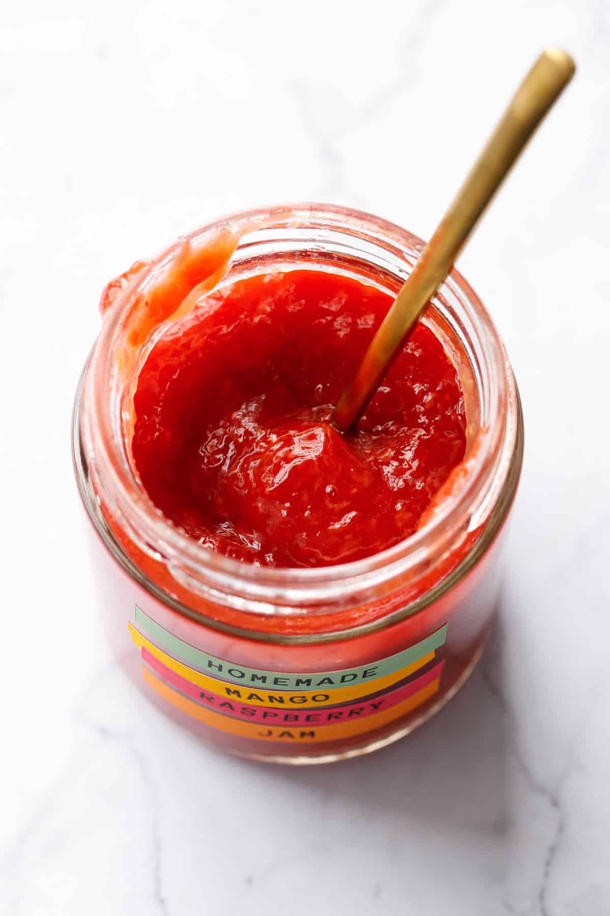 Looking down into an open jar of Mango Raspberry Jam, showing the smooth texture and bright color.