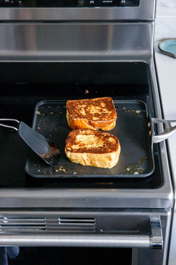 Stuffed French toasts on a nonstick skillet on the stove, after flipping so the golden brown color is shown.