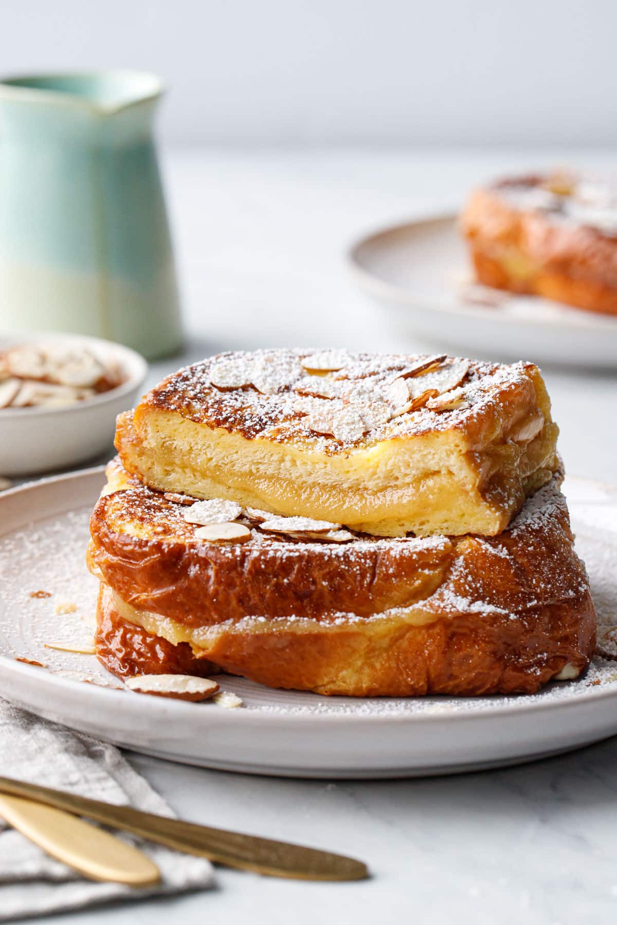 Stacked Marzipan-Stuffed French Toast on a white plate, one piece cut in half to show the gooey almond filling.