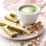 Fingers of Matcha Pistachio Shortbread on a ceramic plate with a mug of matcha and pistachios scattered around