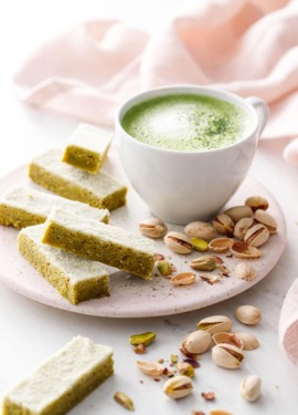 Fingers of Matcha Pistachio Shortbread on a ceramic plate with a mug of matcha and pistachios scattered around