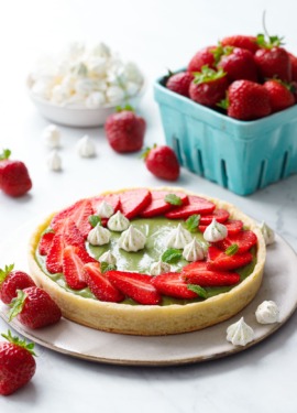 Matcha Strawberry Tart on a marble background, with turquoise basket of strawberries and a bowl of mini meringue kisses.