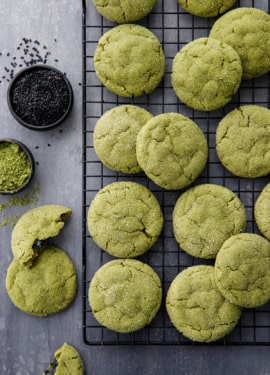 Overhead shot with a cooling rack with rows of matcha sugar cookies, bowls of matcha powder and black sesame seeds.