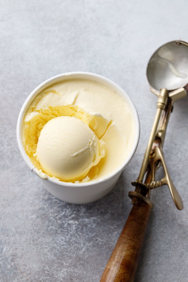 Scoop of olive oil ice cream in a paper ice cream container with vintage ice cream scoop