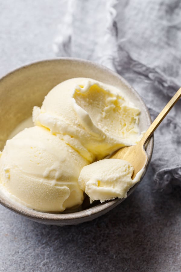 Slightly melted scoops of olive oil ice cream with a spoonful on a gold spoon resting on the bowl