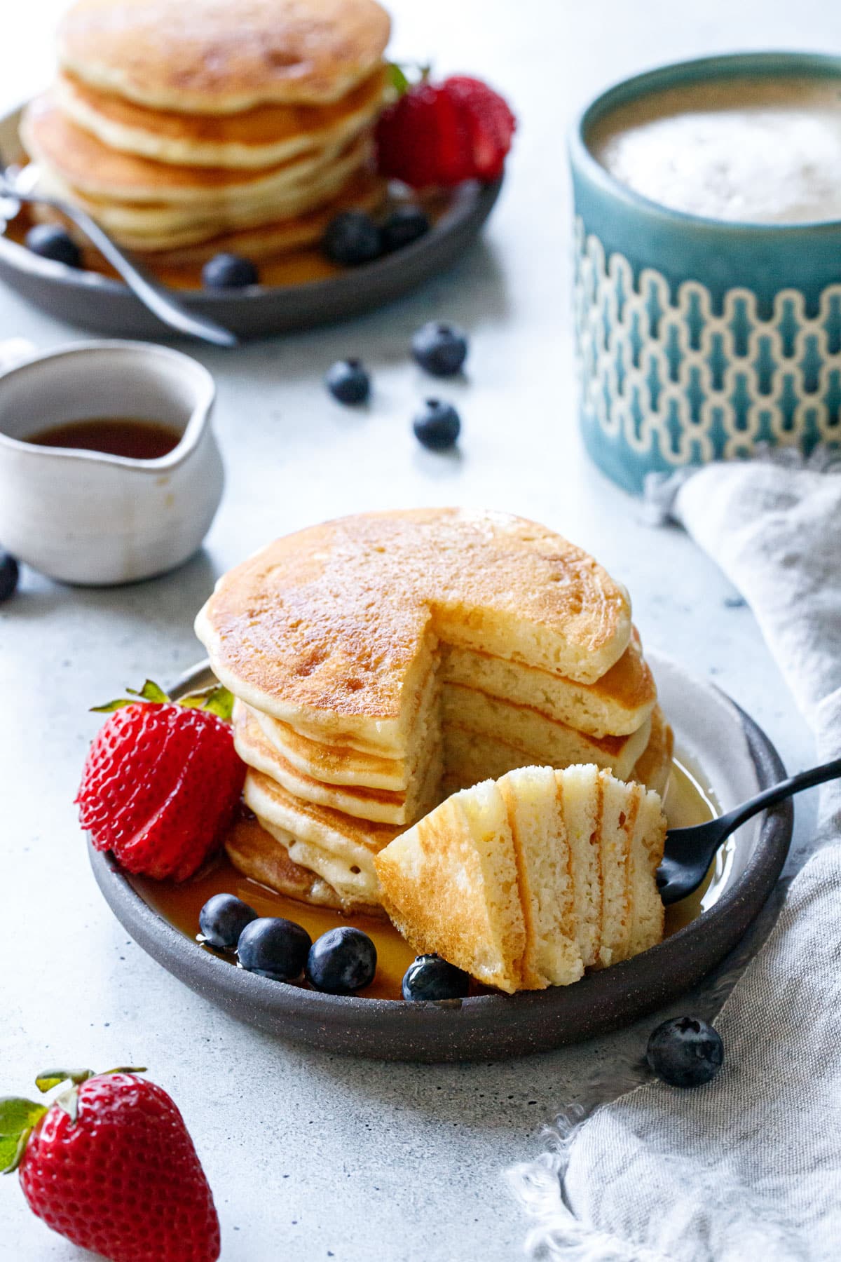 Stack of Olive Oil Pancakes with a wedge cut out on a fork to show the fluffy interior texture.