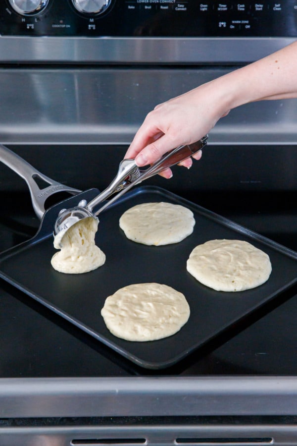 Scooping raw pancake batter onto a griddle pan.