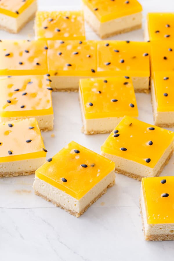 Passionfruit Cheesecake Bars cut into perfect squares, with a crisp layer of bright yellow passionfruit gelatin on top with black seeds.