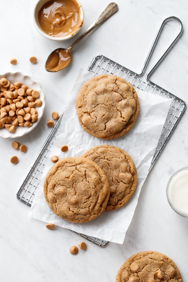 Overhead, Salted Peanut Butter Chip Cookies on a small wire rack, with peanut butter and peanut butter chips and a glass of milk around the edges.