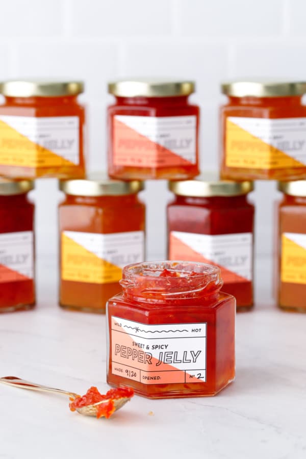 Jars of red and orange pepper jelly with labels stacked on white