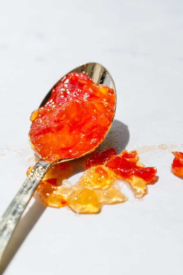 Closeup to show texture of small gold spoon with red pepper jelly