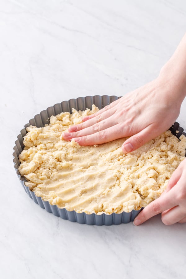 Hand pressing the shortbread dough into a fluted tart pan.