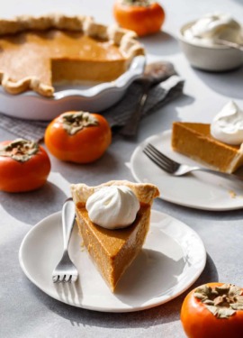 Slices of Persimmon Pie on white plates, what's left of the full pie in the background along with a few Fuyu persimmons.