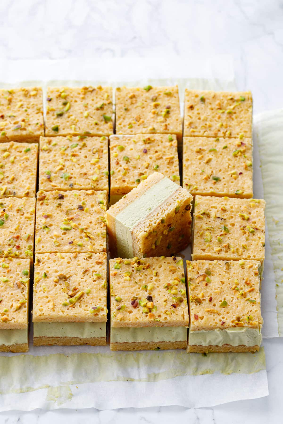 Cut squares of Pistachio Blondie Ice Cream Sandwiches on parchment paper, one square propped on its side to see the layers.