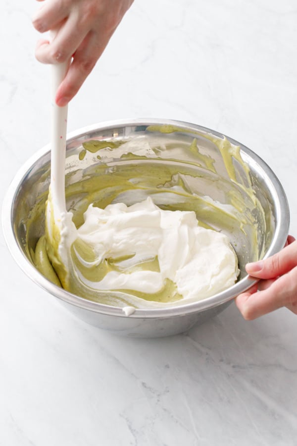 Folding the whipped cream into the pistachio mixture in a metal mixing bowl.