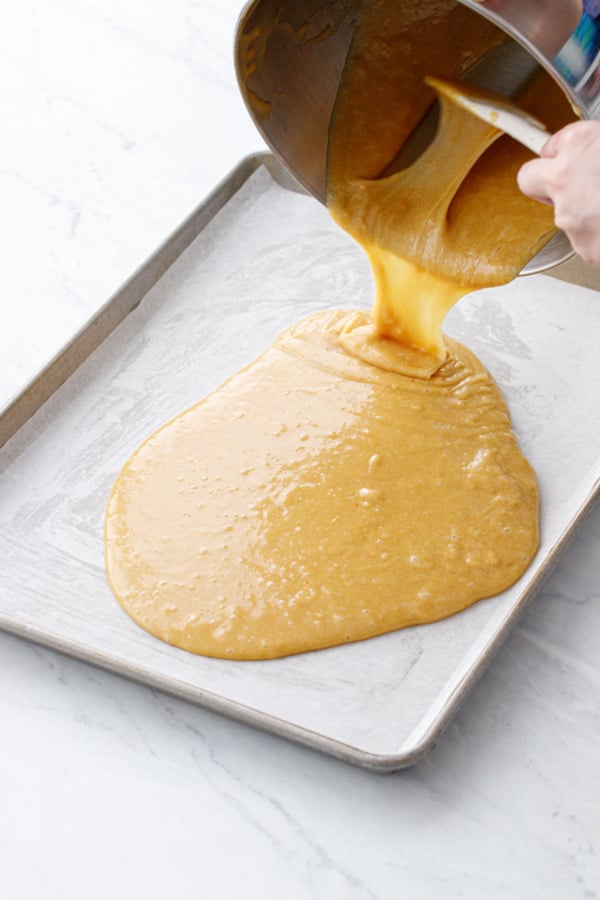 Pouring the blondie batter into a parchment-lined half-sheet pan.