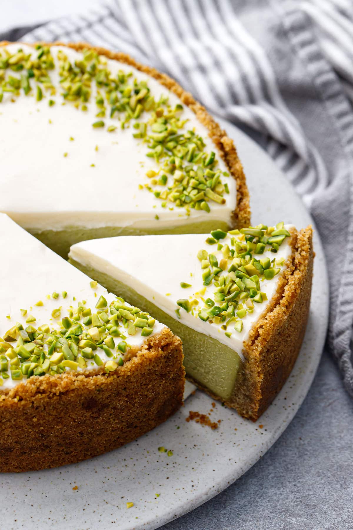 Slice of Pistachio Sour Cream Cheesecake on a flat cake plate, slice pulled out slightly to show the green-tinted filling.