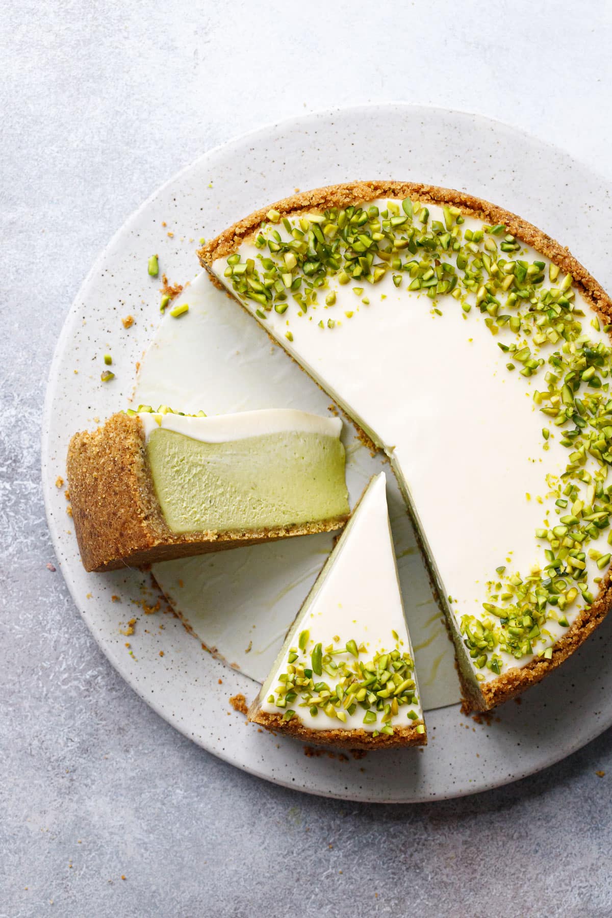 Overhead, slices of Pistachio Sour Cream Cheesecake, one on its side to show the green pistachio filling and sour cream layers.