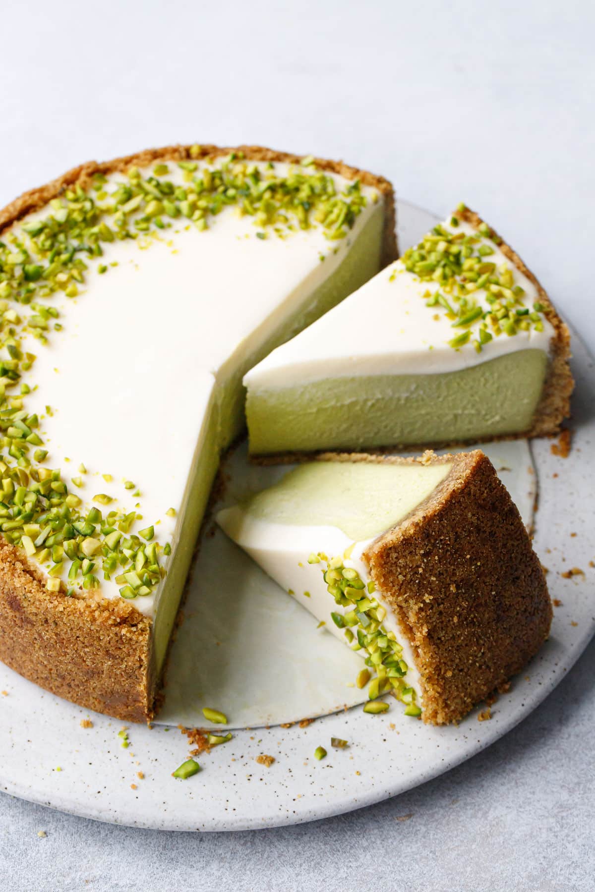 Cut slices of Pistachio Sour Cream Cheesecake on a flat cake plate, one slice tipped on its side.