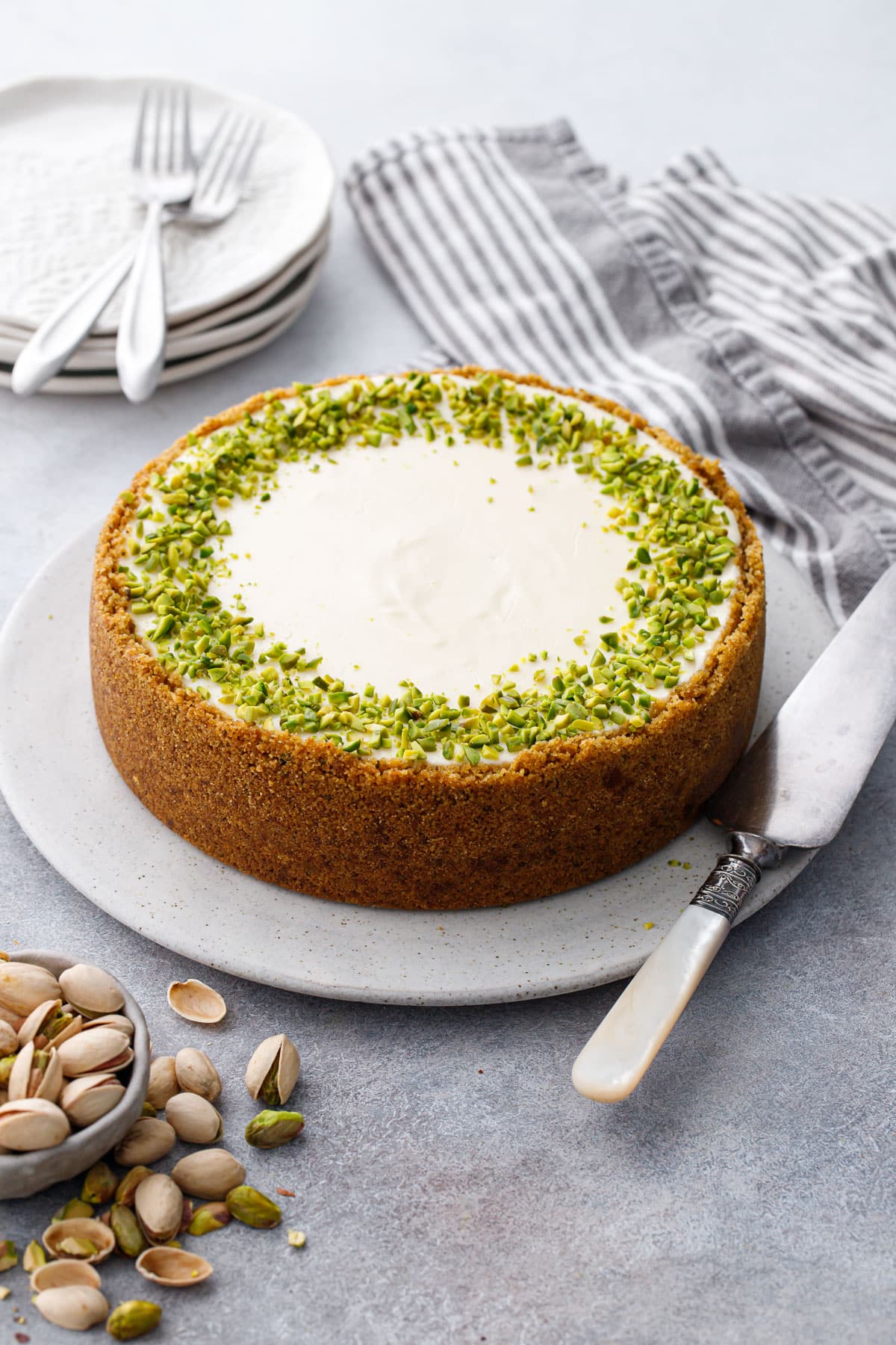 Whole Pistachio Sour Cream Cheesecake before slicing, showing the vanilla wafer crust, sour cream topping, and chopped pistachio garnish.