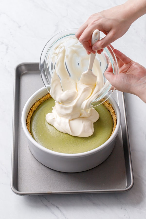 After baking and cooling slightly, pouring the sour cream topping onto the top of the green pistachio cheesecake.