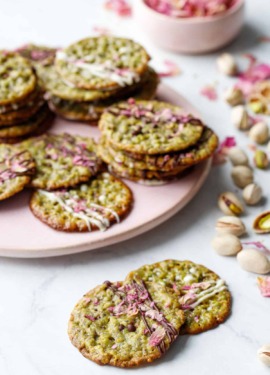 Pistachio Florentine Cookies on a pink plate with scattered pistachios and rose petals around.