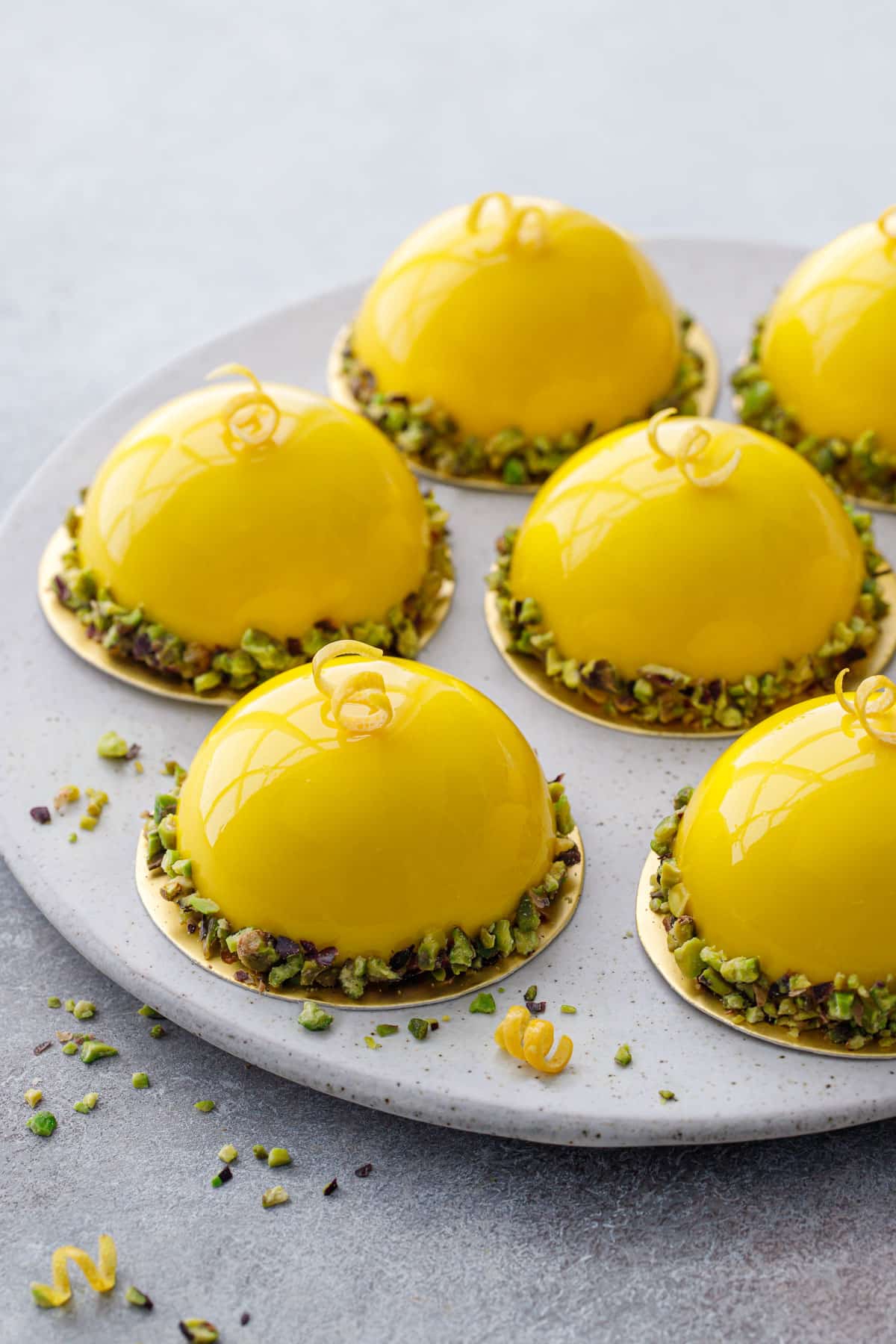 Plate with dome-shaped Pistachio & Meyer Lemon Mousse Cakes with bright yellow shiny mirror glaze.