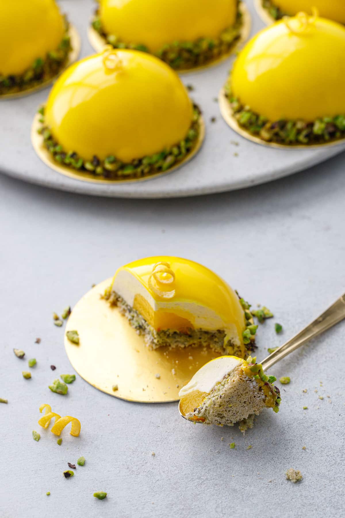 Pistachio & Meyer Lemon Mousse Cake on a gold cake board with a bite taken out of it so it shows the distinct layers and textures inside.