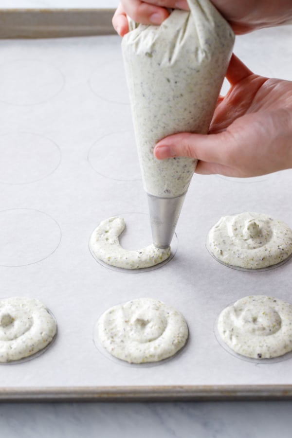 Piping pistachio dacquoise into rounds on a parchment-lined cookie sheet.