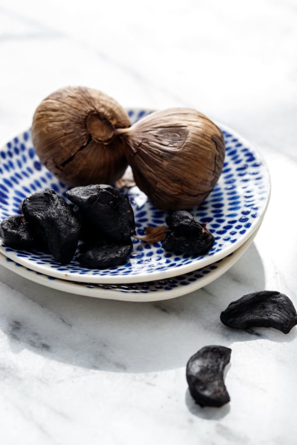 Cloves (both peeled and unpeeled) of black garlic on a blue painted ceramic dish.