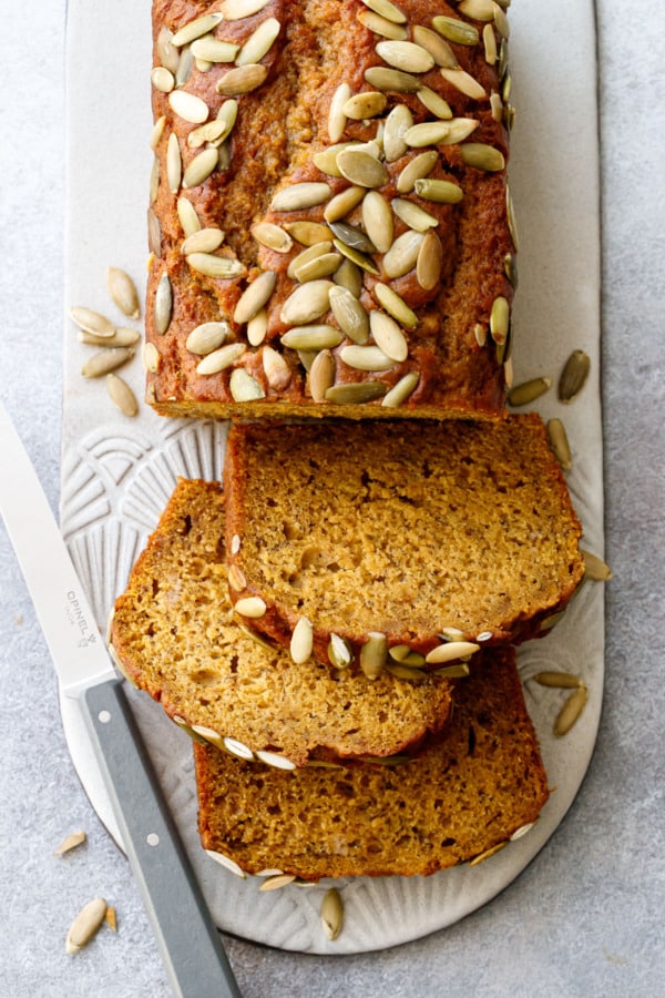 Overhead, slices of Spiced Pumpkin Banana Bread on a ceramic serving plate and gray knife.