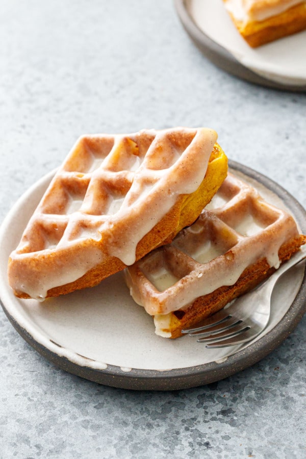 Plate with two stacked pumpkin donut waffles with a vanilla cardamom glaze dripping over the sides.