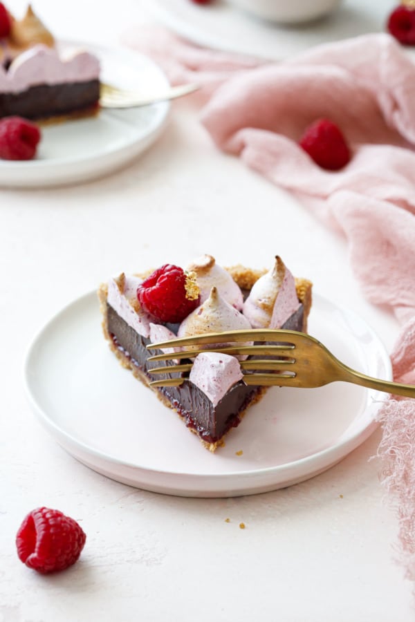 Perfect triangular slice of Chocolate Raspberry S'mores Tart on a pink dessert plate, gold fork taking a bite off of the tip.