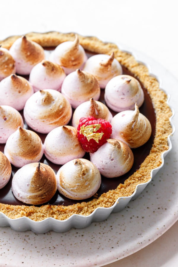Chocolate Raspberry S'mores Tart with piped kisses of blush-pink raspberry marshmallow meringue, topped with a single fresh raspberry with gold leaf.