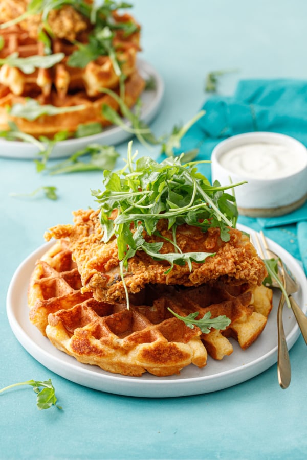 Two plates with Savory Cheddar Cheese Waffles topped with fried chicken and a pile of baby arugula