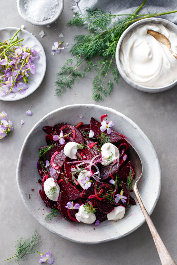Overhead shot of cumin-spiced beet salad with bowls of yogurt and radish flowers on the side