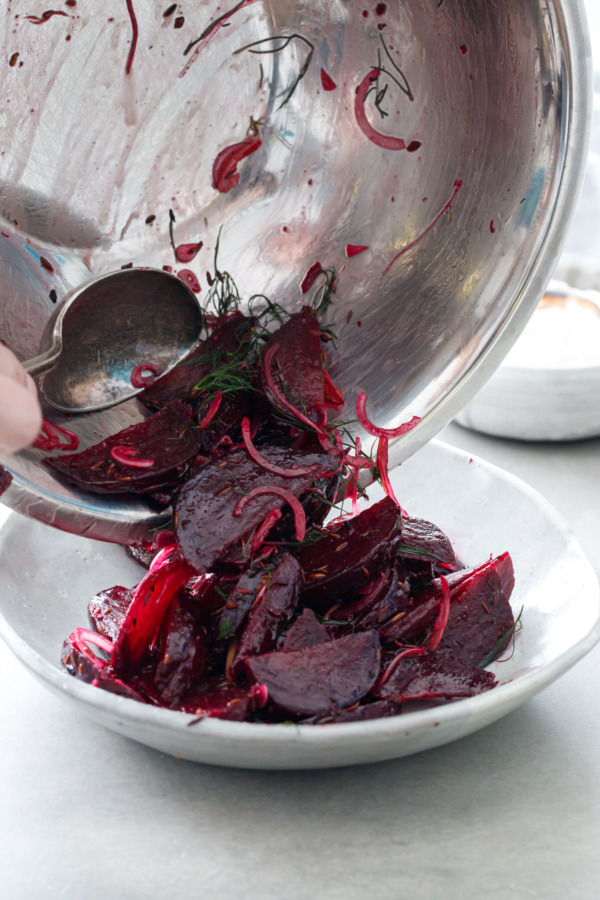 Beets tossed with spiced cumin oil, red onion and preserved lemon being poured into a serving bowl