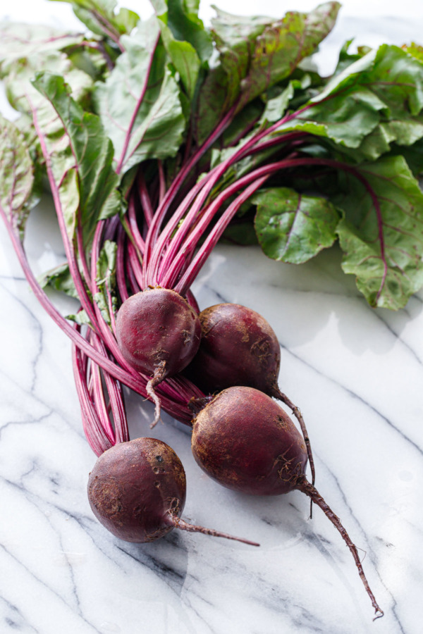 Bunch of fresh red beets with green leaves on a marble surface