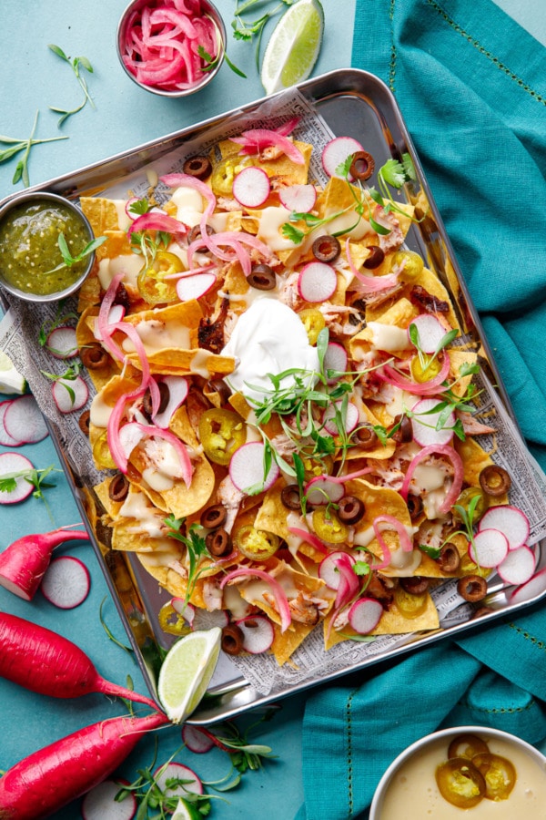 Overhead, sheet pan of Loaded Smoked Chicken Nachos with radishes, micro cilantro on a turquoise background